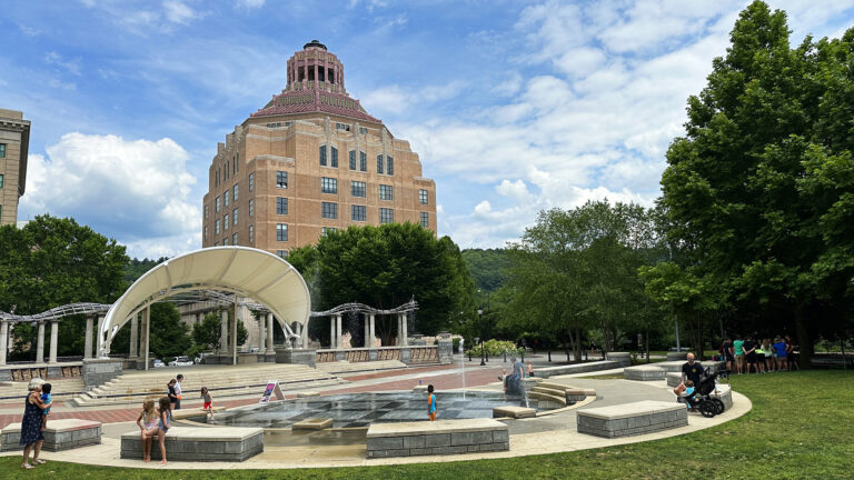 City Hall in background with Splasheville and residents in foreground on a bright smmer day