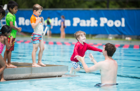 young child in red swim shirt jumping into the arms of man in pool