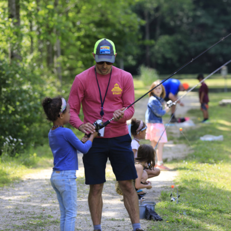 male parks and recreation staff with young female child with fishing pole