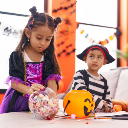 two children wearing costumes decorating pumpkins