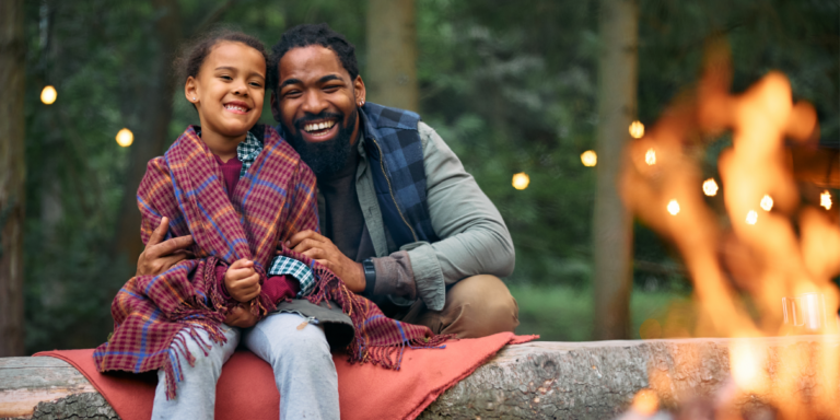 fall scene with African American man and young girl sitting on a log by the fire