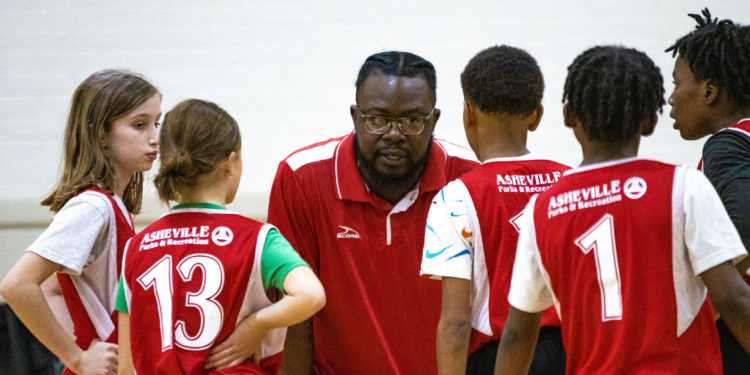 coach wearing red shirt speaking to two young girls and three young boys, also wearing red shirts