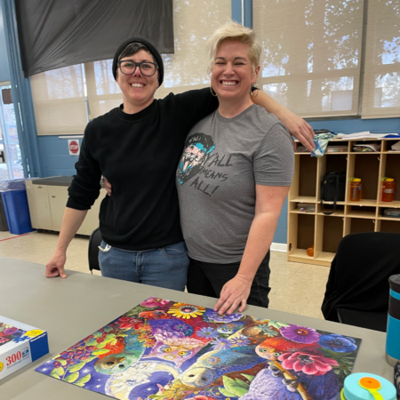 woman in black shirt and woman in gray shirt proud of completed puzzle on table